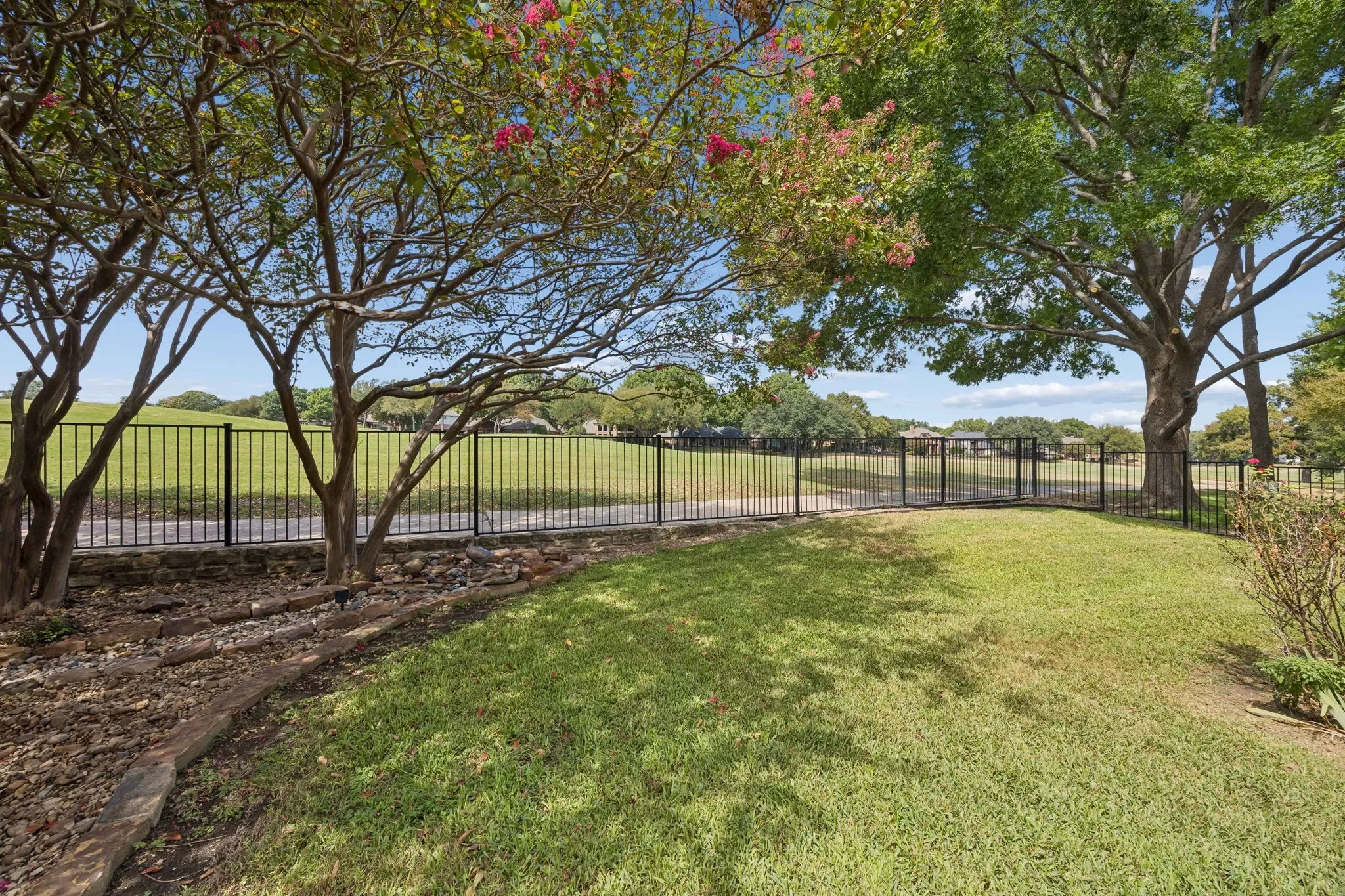 Looking from the flagstone pathway across the yard to the golf course and walking path behind the home. There is a gate in the fence that leads to the walking path.