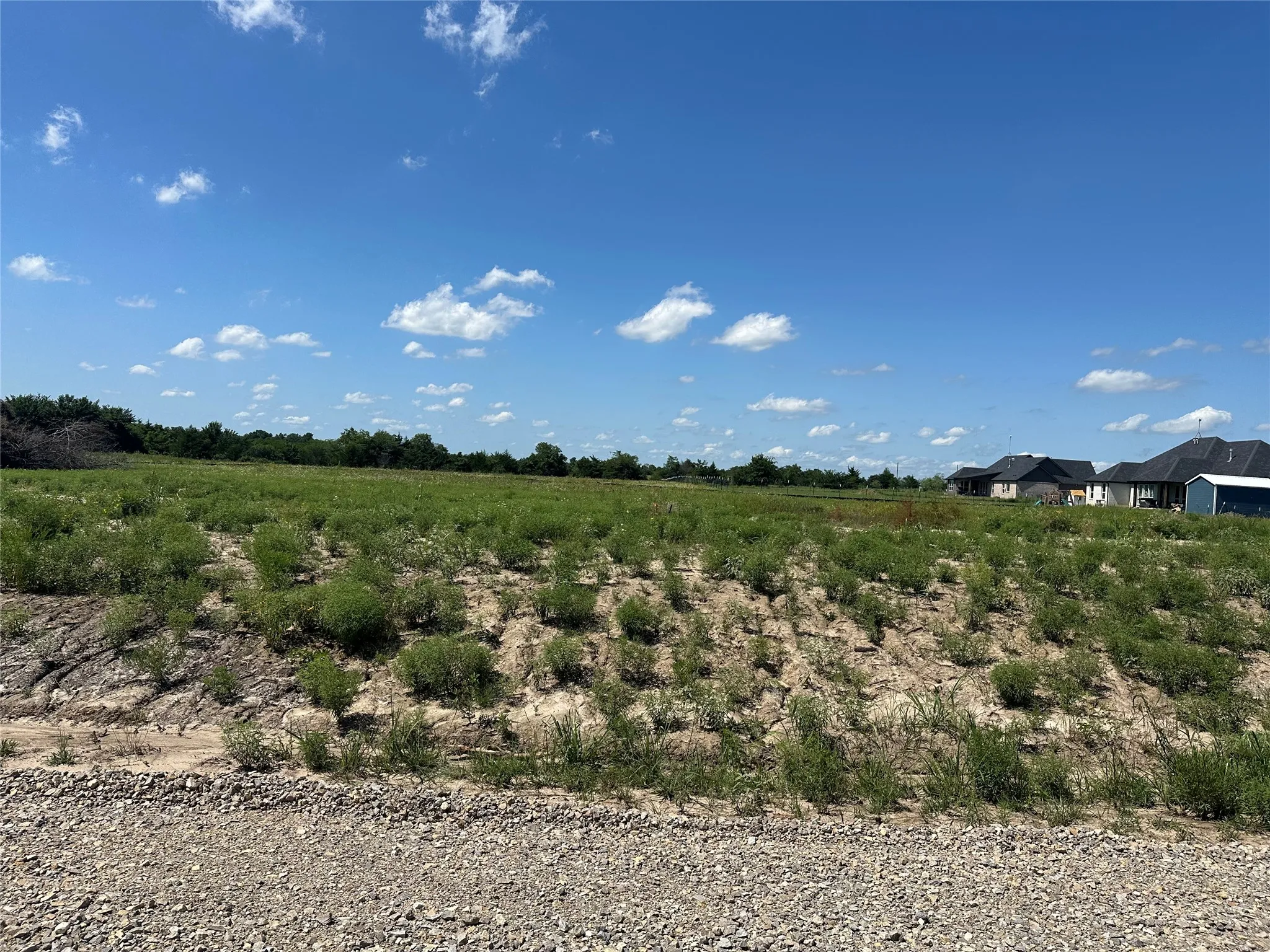 Expansive lot featuring a gravel foreground, gently sloped terrain, and distant residential structures