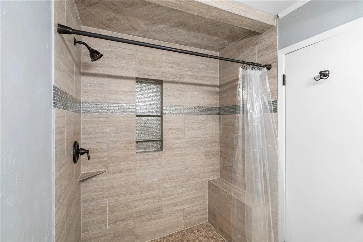 Tiled shower featuring a built-in bench, integrated shelving, and bronze fixtures