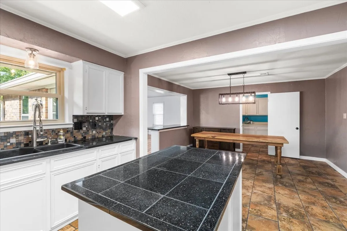 Kitchen featuring white cabinetry, black tiled countertops, a mosaic tile backsplash, and a double basin sink