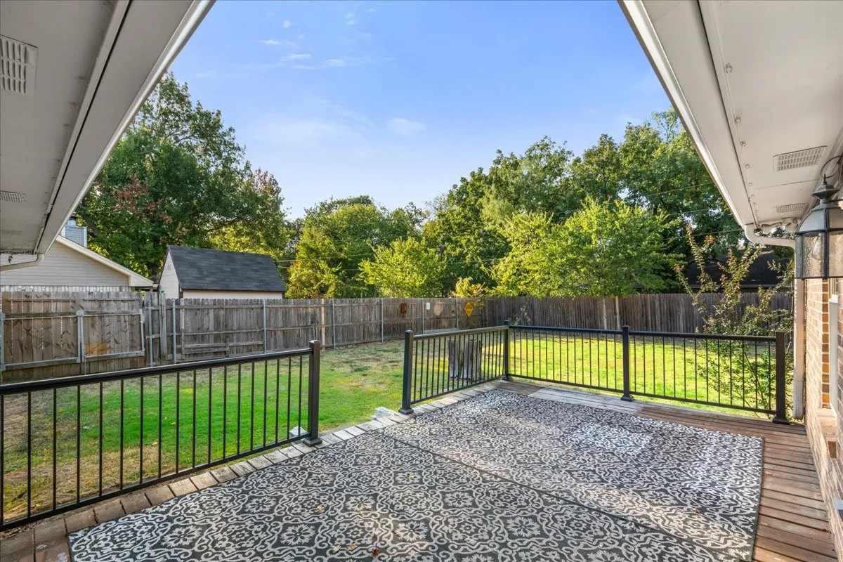 Covered deck with wood-finish flooring, black metal railings, brick exterior siding, and a grass lawn