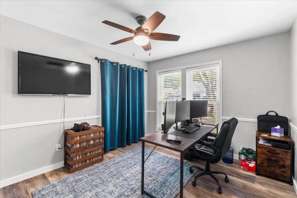 Wood-finish flooring, ceiling fan, natural light from multiple windows, and two-tone wall treatment