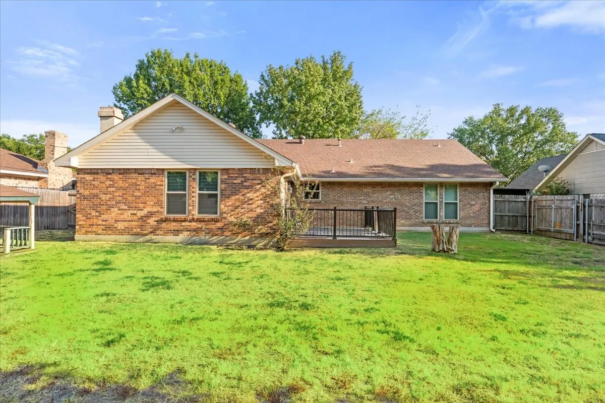 Expansive backyard featuring a wood deck with black railing, brick exterior, and a well-maintained lawn