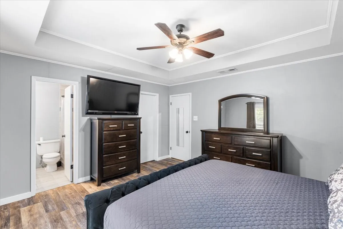Tray ceiling with crown molding, wood-finish flooring, ceiling fan, and white interior doors