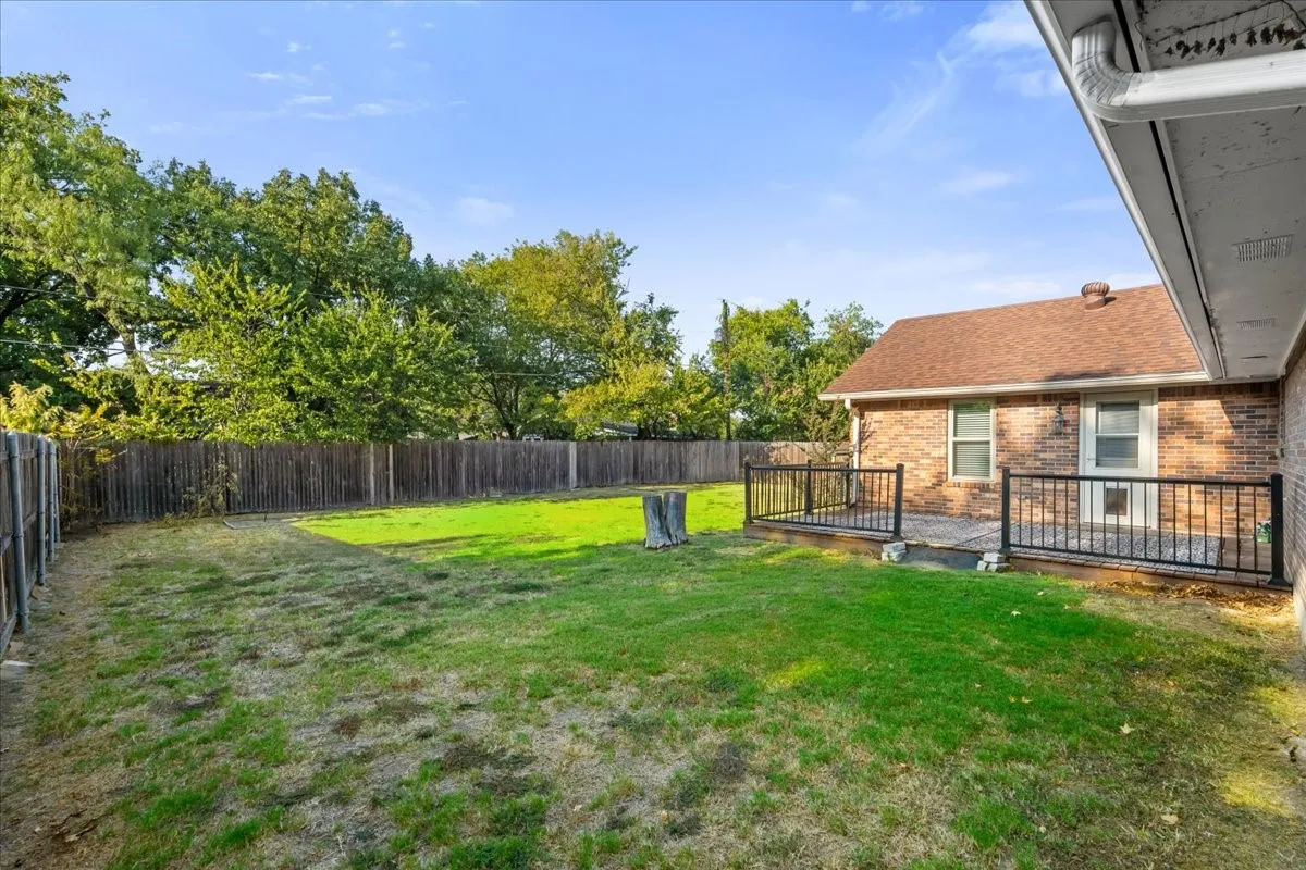 Expansive backyard featuring a wood privacy fence, a brick exterior, a patio with dark railings, and a shingled roof
