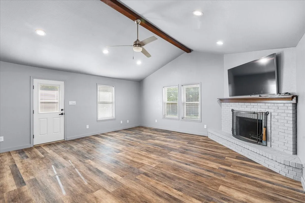 Vaulted ceiling with exposed wood beam, recessed lighting, wood-finish flooring, brick fireplace with wood mantel, and a ceiling fan