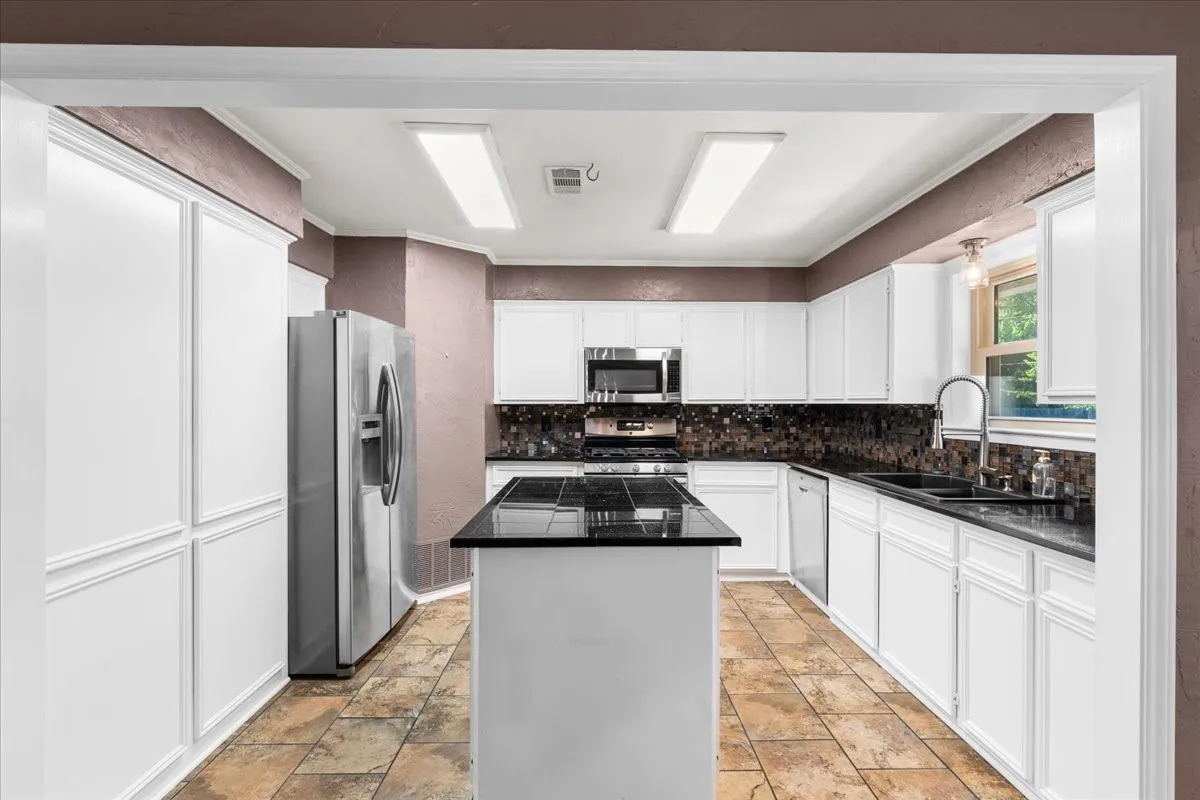 Kitchen featuring white cabinetry, a central island with a dark countertop, stainless steel appliances, a dark tile backsplash, and tile flooring