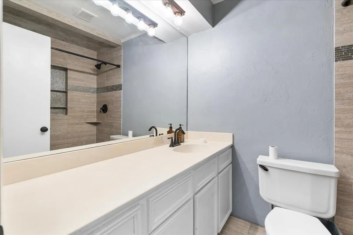 White vanity with a single basin sink, wall-mounted mirror, and overhead lighting