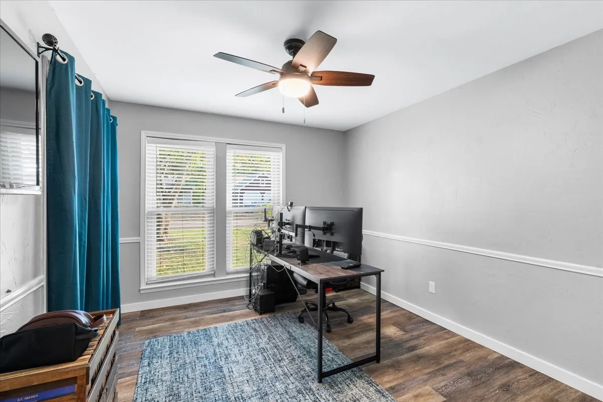 Wood-finish flooring, white trim, dual windows with blinds, ceiling fan with integrated lighting, and chair rail molding
