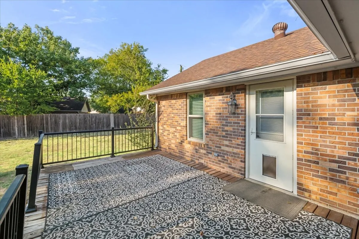 Wood deck with black metal railing, brick exterior, and a shingle roof
