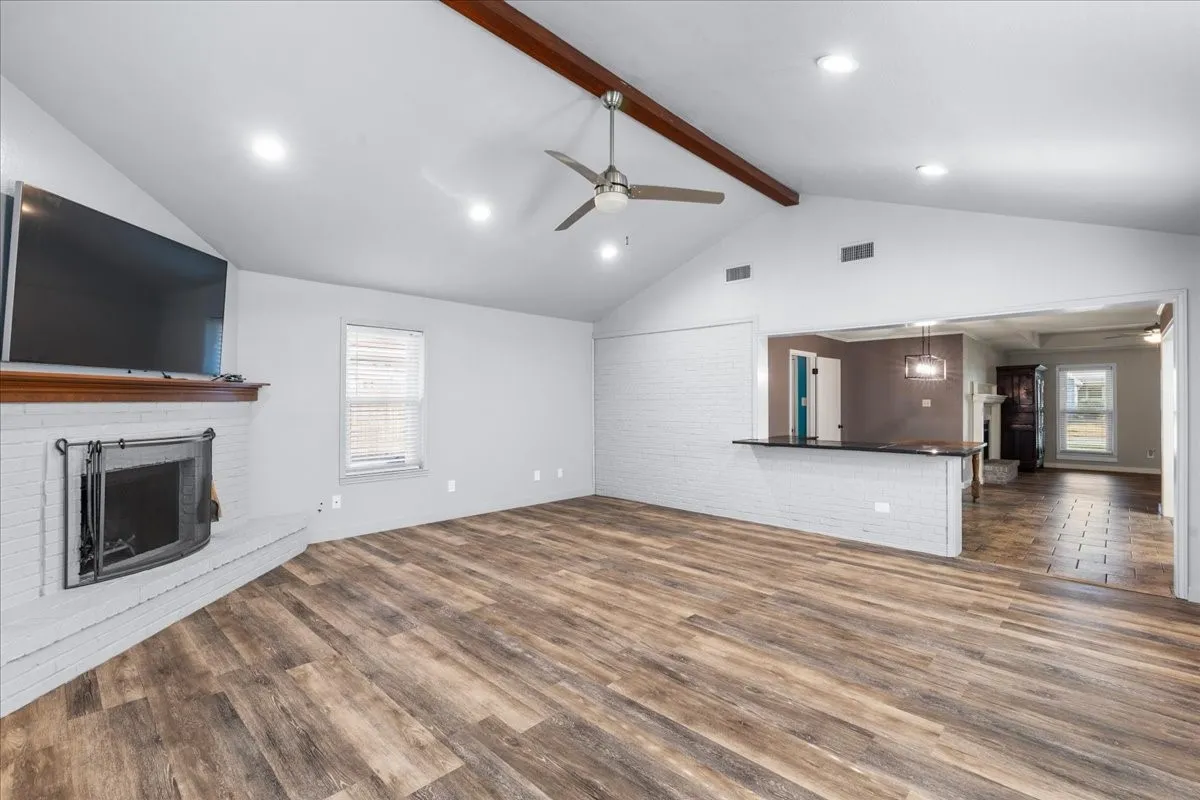 Vaulted ceiling with exposed wood beam, wood-finish flooring, corner fireplace, recessed lighting, and a breakfast bar with a dark countertop