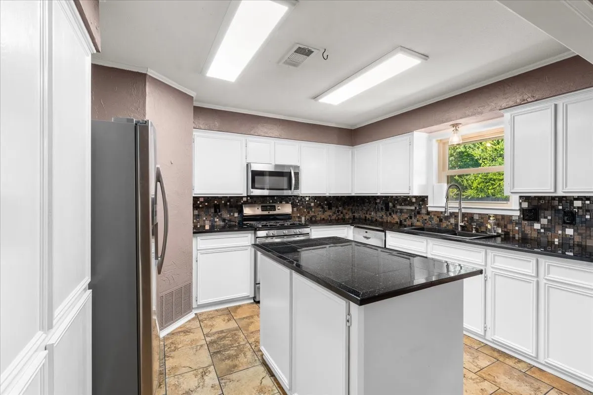 Kitchen featuring an island, white cabinetry, dark countertops, a tile backsplash, and stainless steel appliances