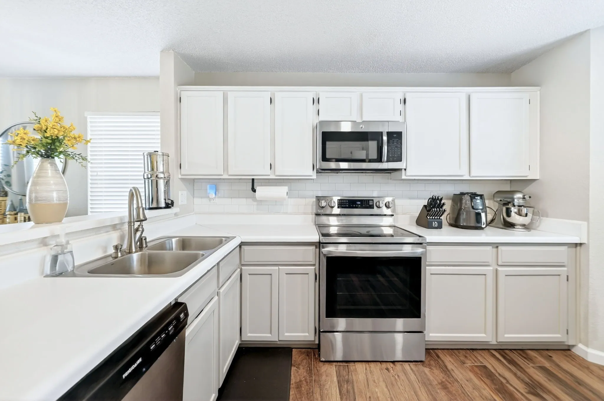 White cabinetry, stainless steel appliances, dual basin sink, white countertops, and wood-finish flooring
