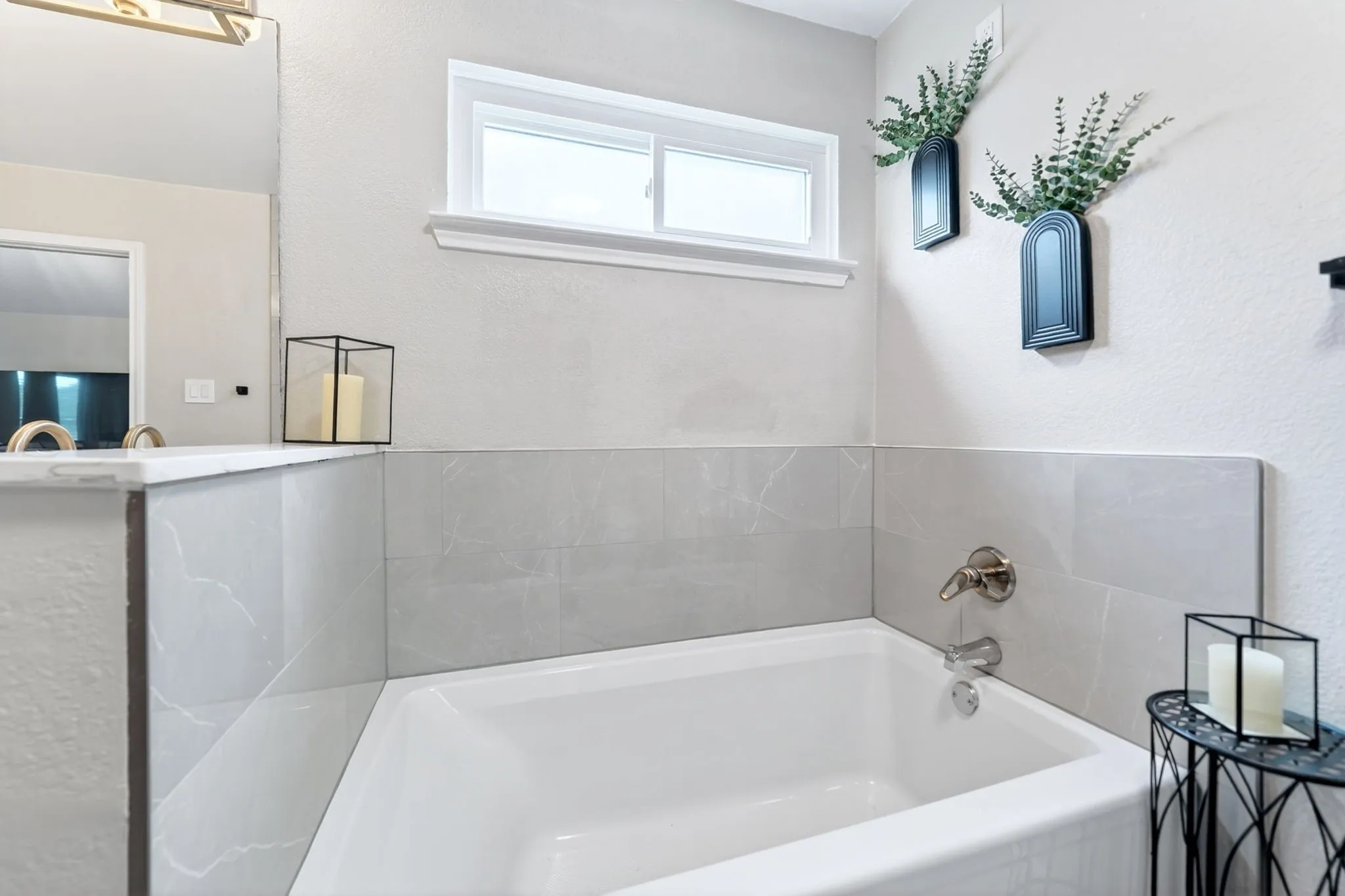 White drop-in bathtub with brushed nickel fixtures, light gray wall tile surround, and a sliding window