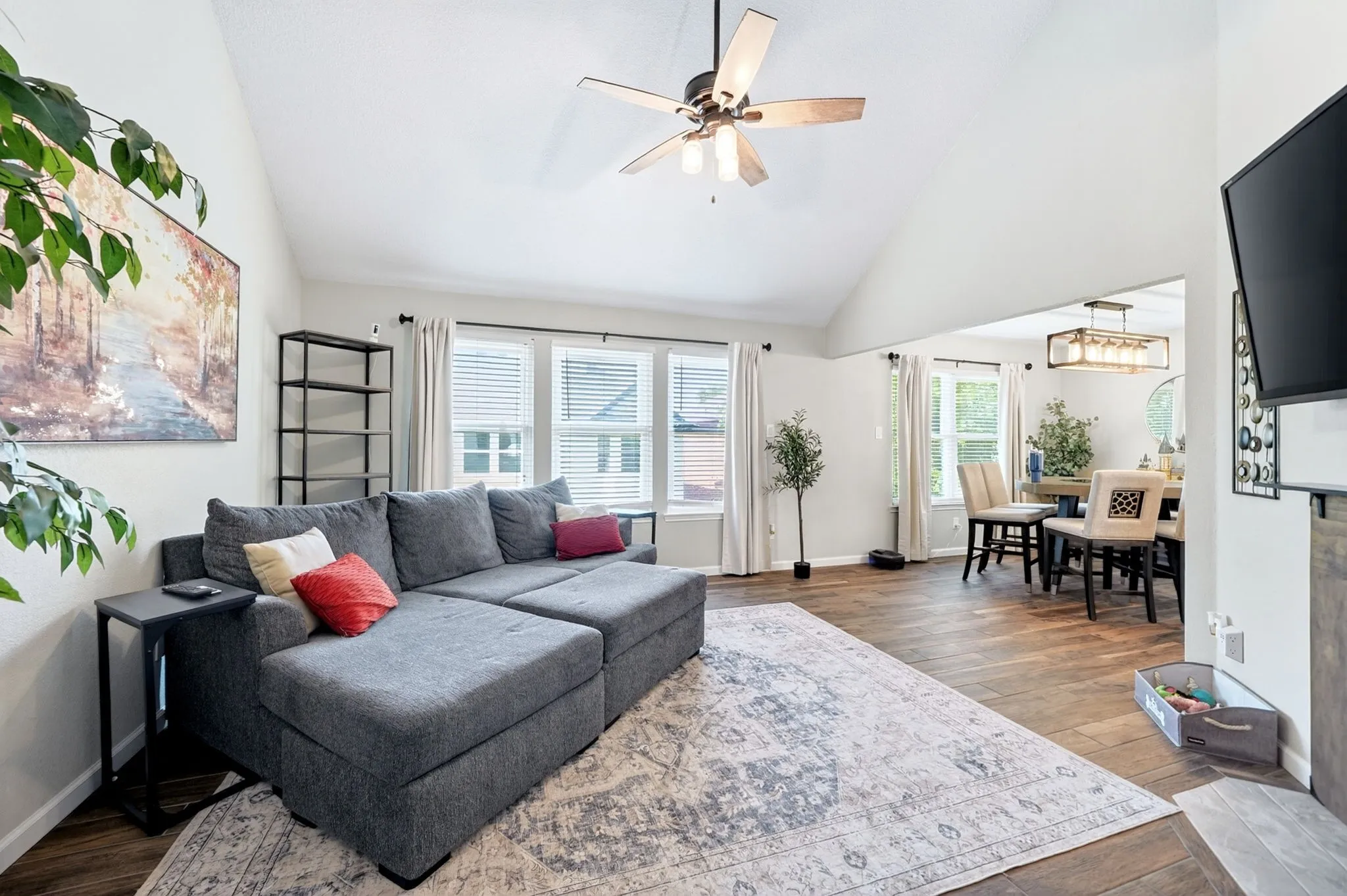 Vaulted ceiling with a ceiling fan, wood-finish flooring, multiple windows with blinds, and an open concept layout
