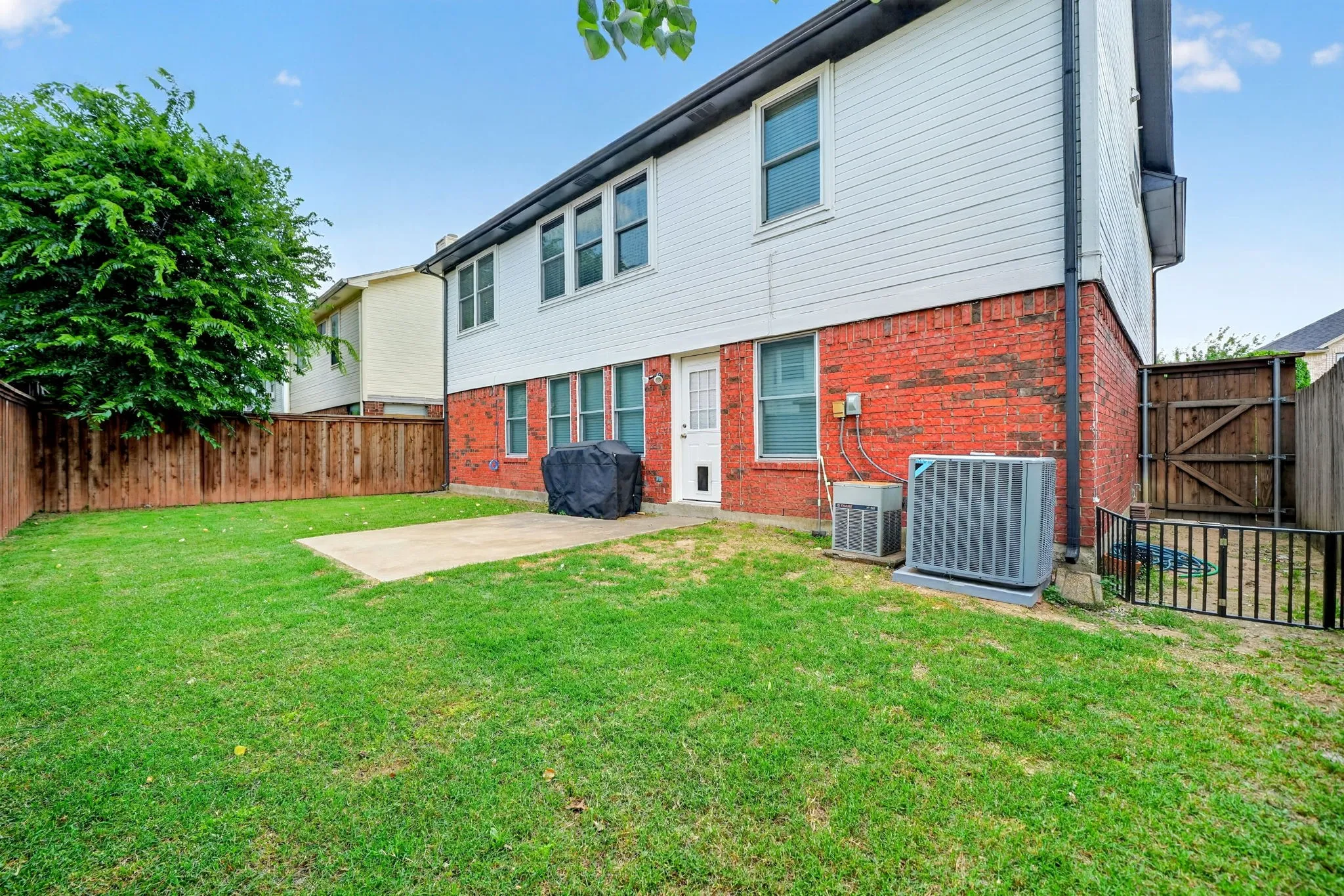 Expansive lawn area with a concrete patio, wood privacy fencing, and a brick and siding exterior