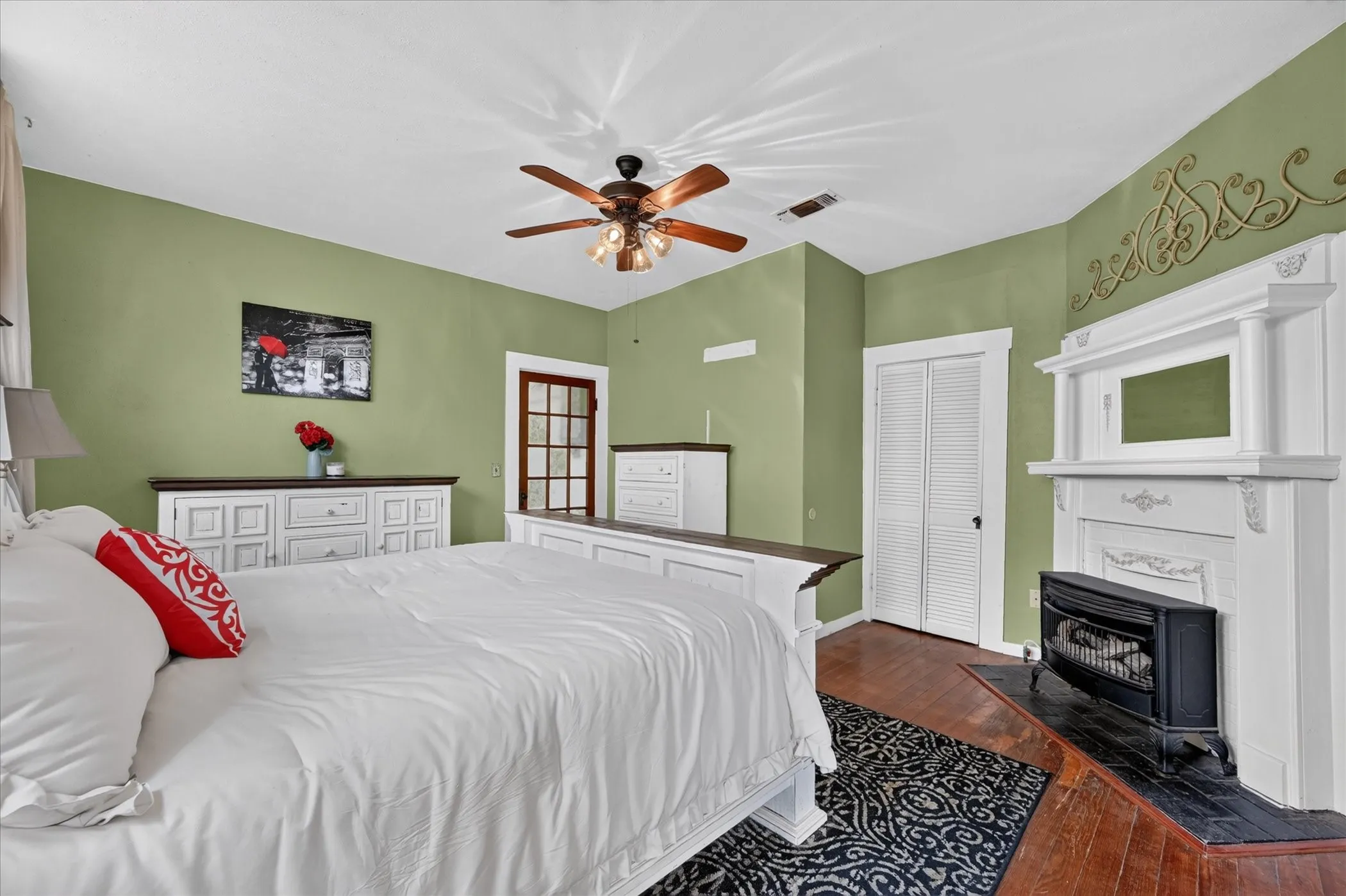 Hardwood flooring, white architectural fireplace with dark hearth, ceiling fan, louvered closet doors, and a glass-paneled door