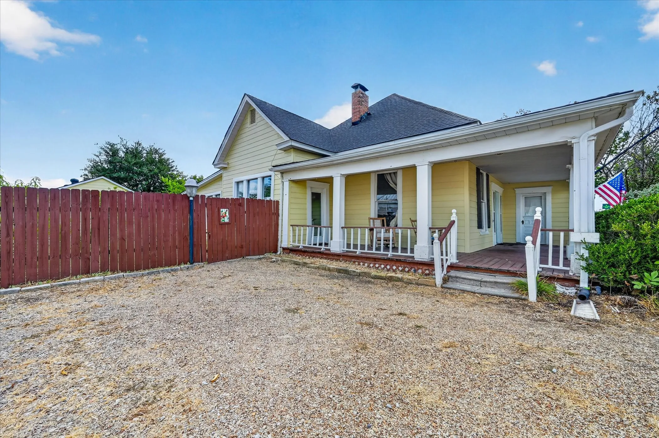Gable roofline, covered front porch, gravel lot, and privacy fence