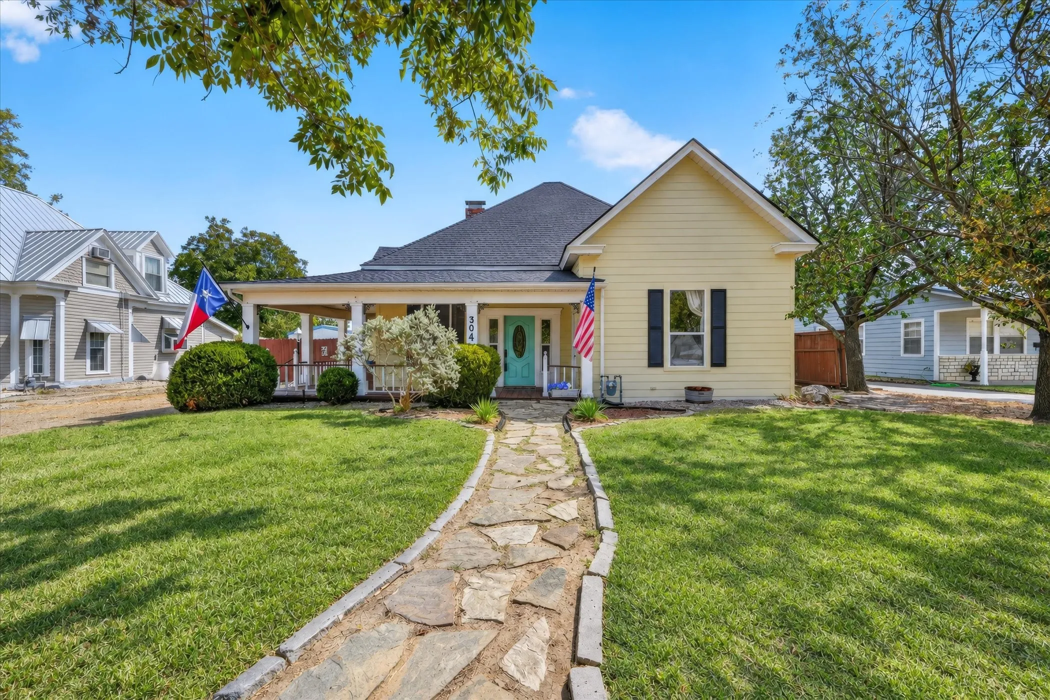 Yellow siding exterior with a dark shingle roof, a covered front porch, and a stone-paver walkway