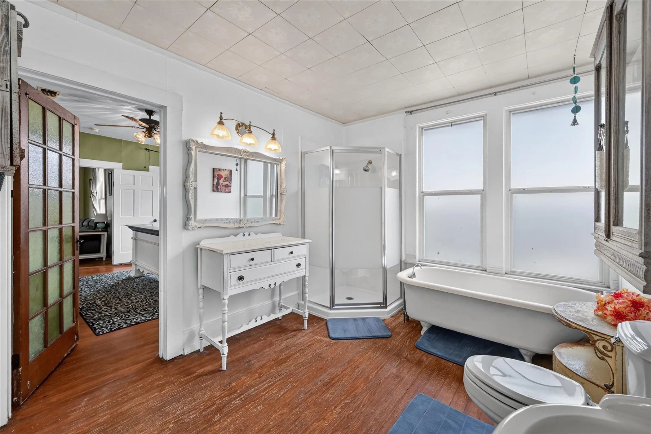 Wood-finish flooring with a white clawfoot tub, clear glass shower enclosure, and white vanity with a framed mirror