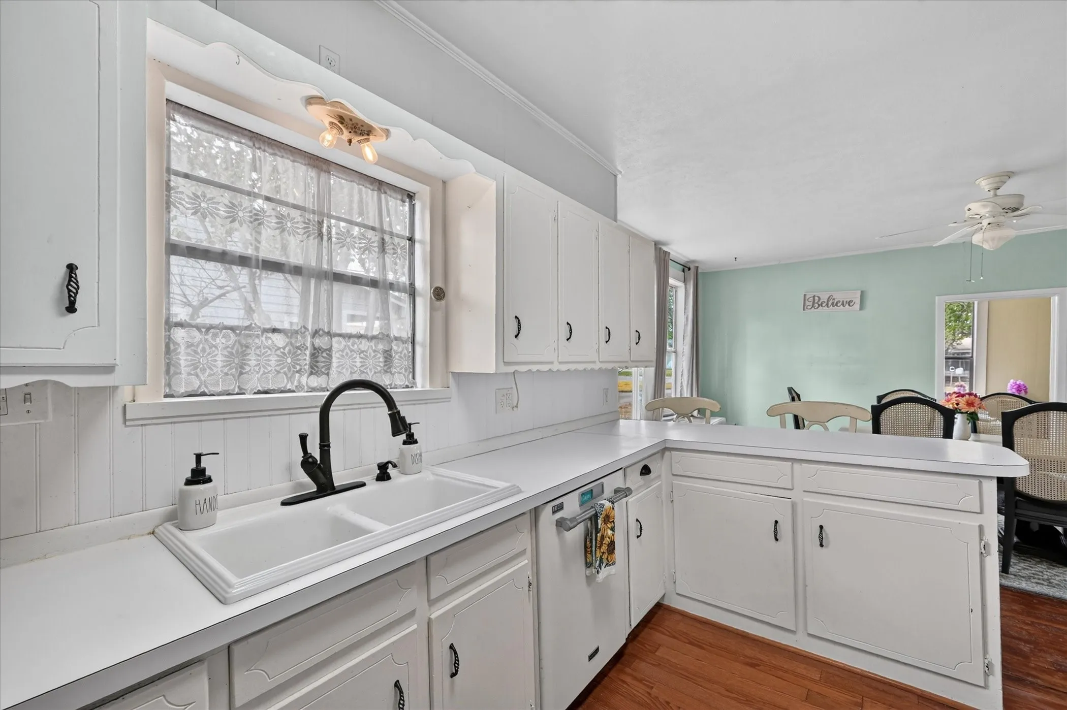 White cabinetry with dark hardware, white countertops, a double basin sink with a matte black faucet, and wood-finish flooring