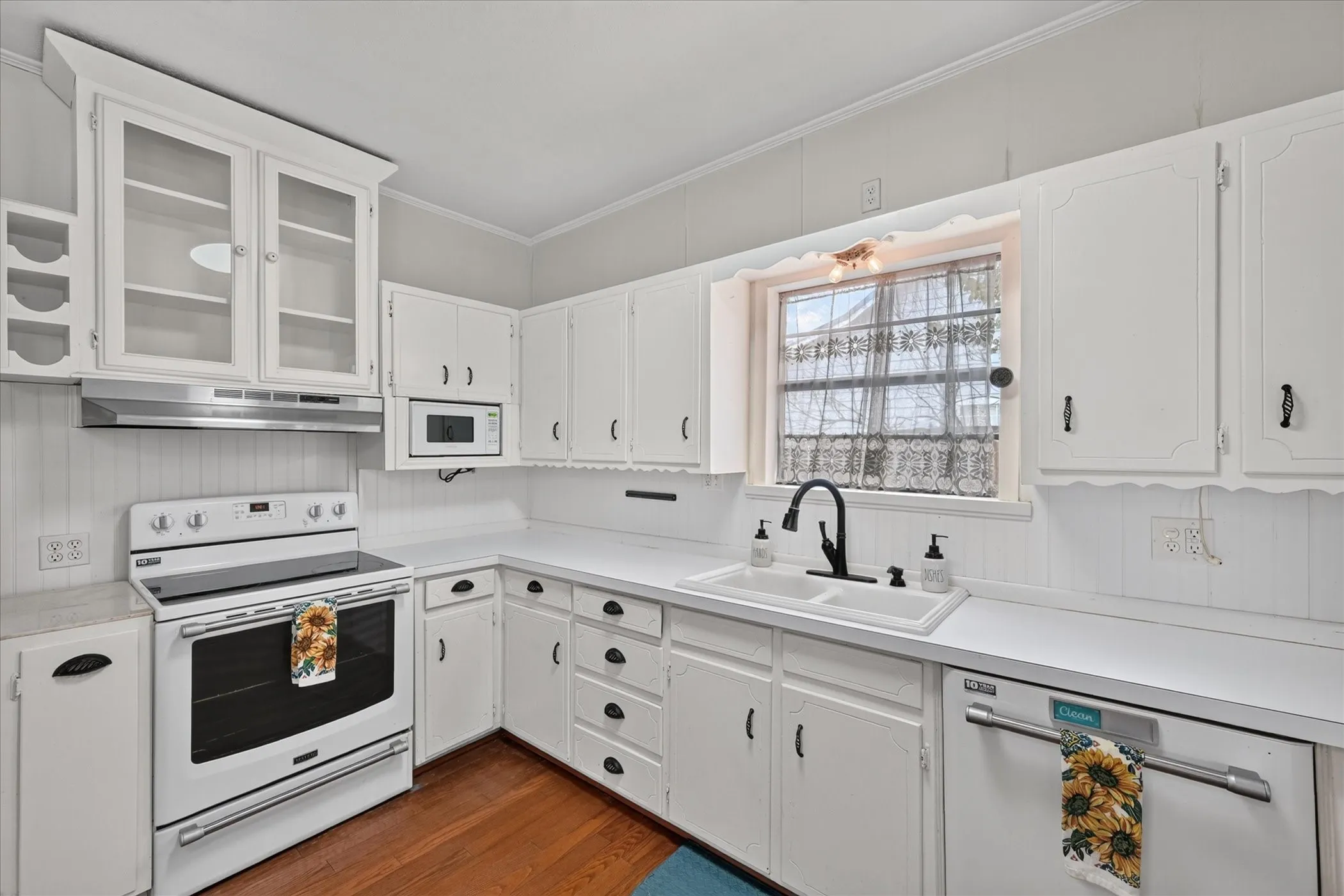 Kitchen featuring white cabinetry, a double basin sink with a matte black faucet, a white electric range, a built-in microwave, and wood-finish flooring