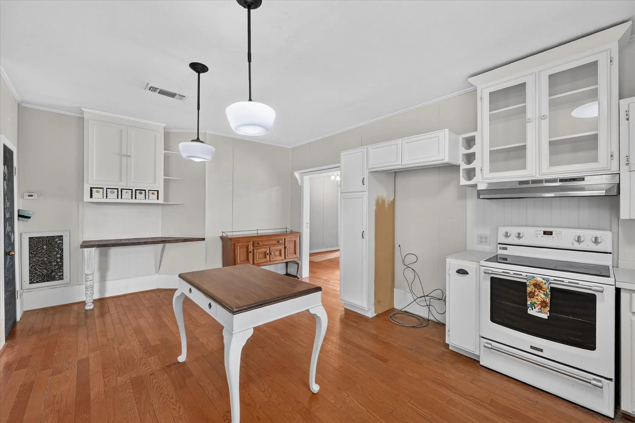 Hardwood-finish flooring, white cabinetry with glass inserts, built-in shelving, pendant lighting, and a white electric range