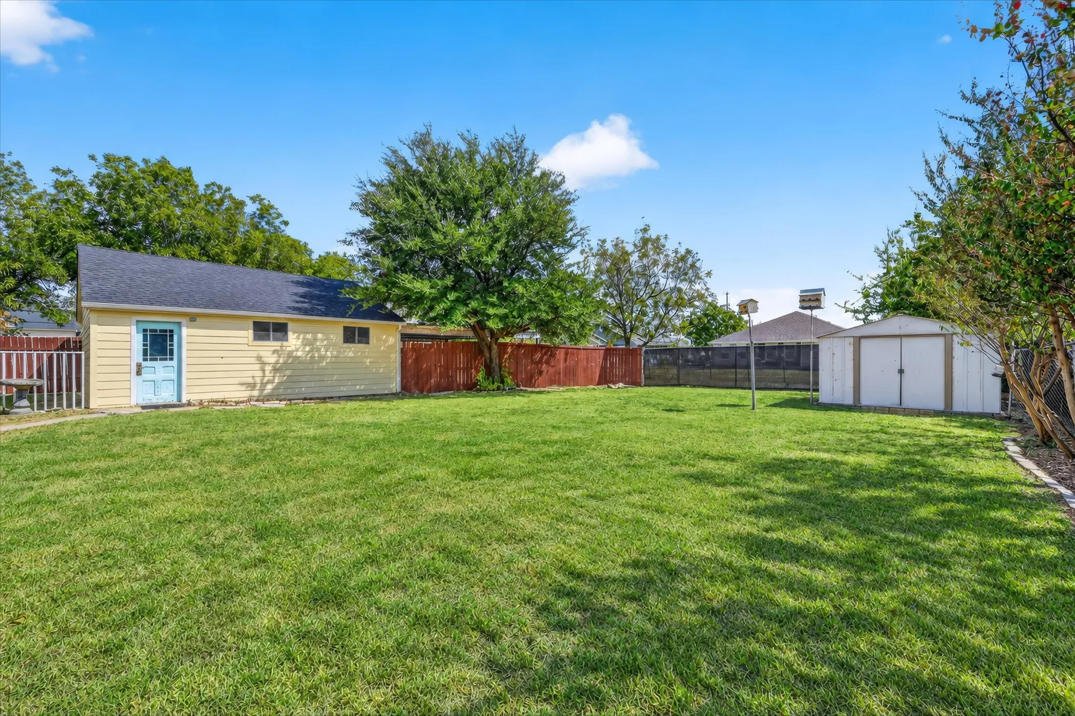 Expansive lawn with a detached auxiliary building, additional storage shed, and mature trees, all enclosed by fencing