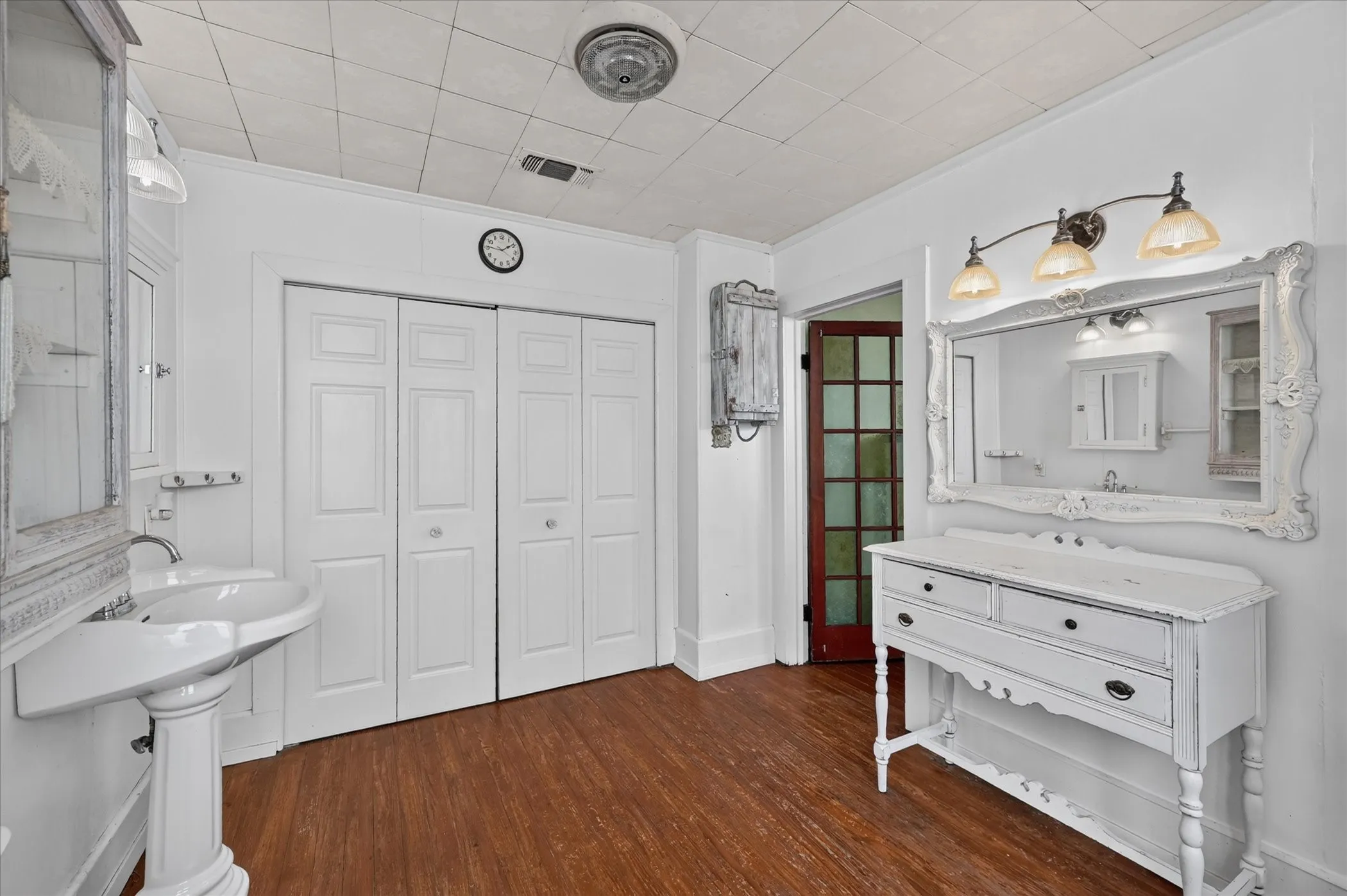 Wood-finish flooring, white pedestal sink, white bi-fold closet doors, and an ornate white framed mirror