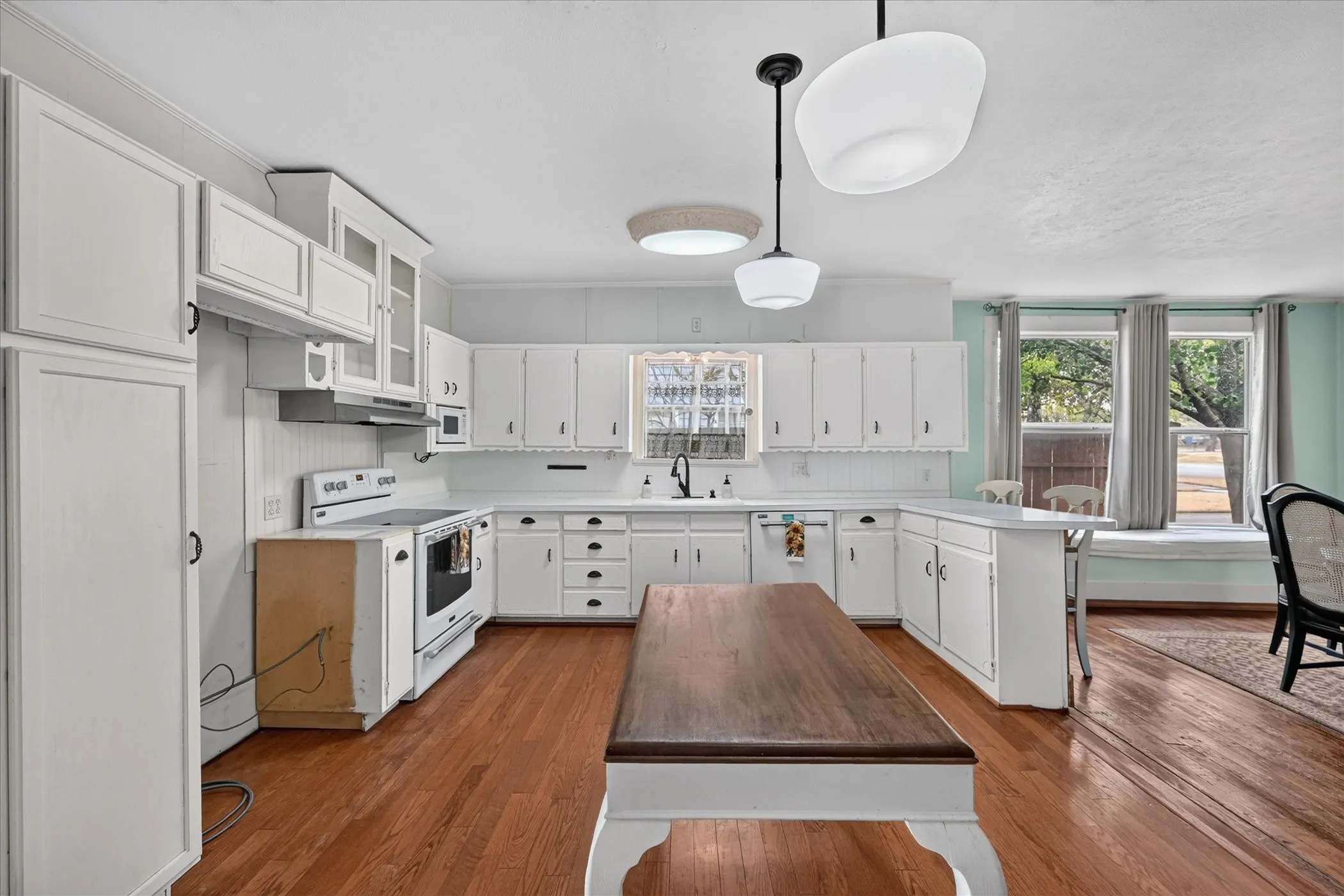 Kitchen featuring white cabinetry, hardwood flooring, a central island, built-in appliances, and a window seat