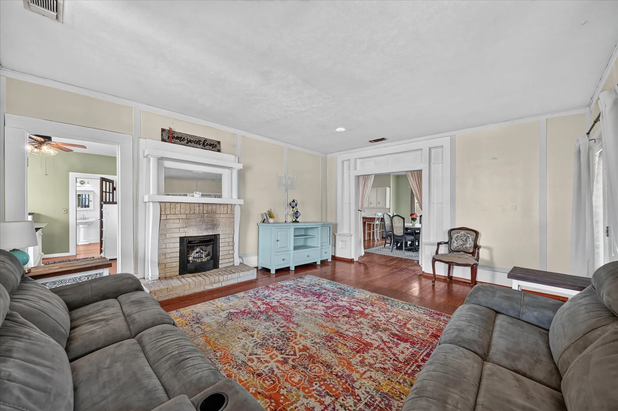 Hardwood flooring, brick fireplace with mantel, decorative trim work, and high ceilings