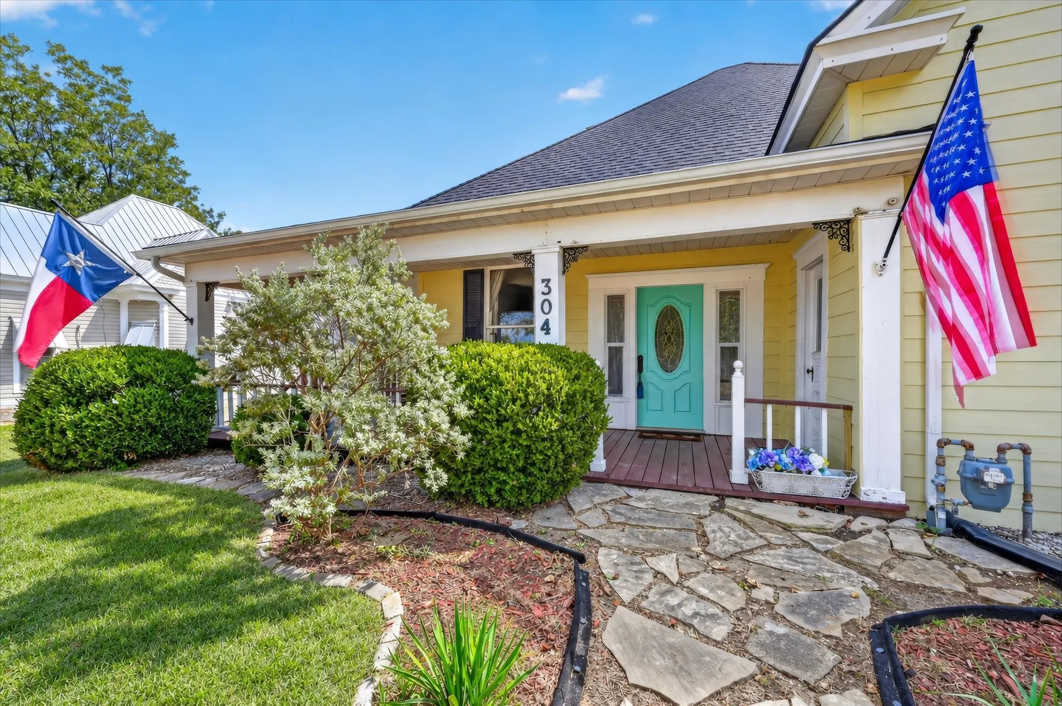 Front elevation featuring a vibrant turquoise front door, covered porch with white columns, stone pathway, and landscaped shrubbery