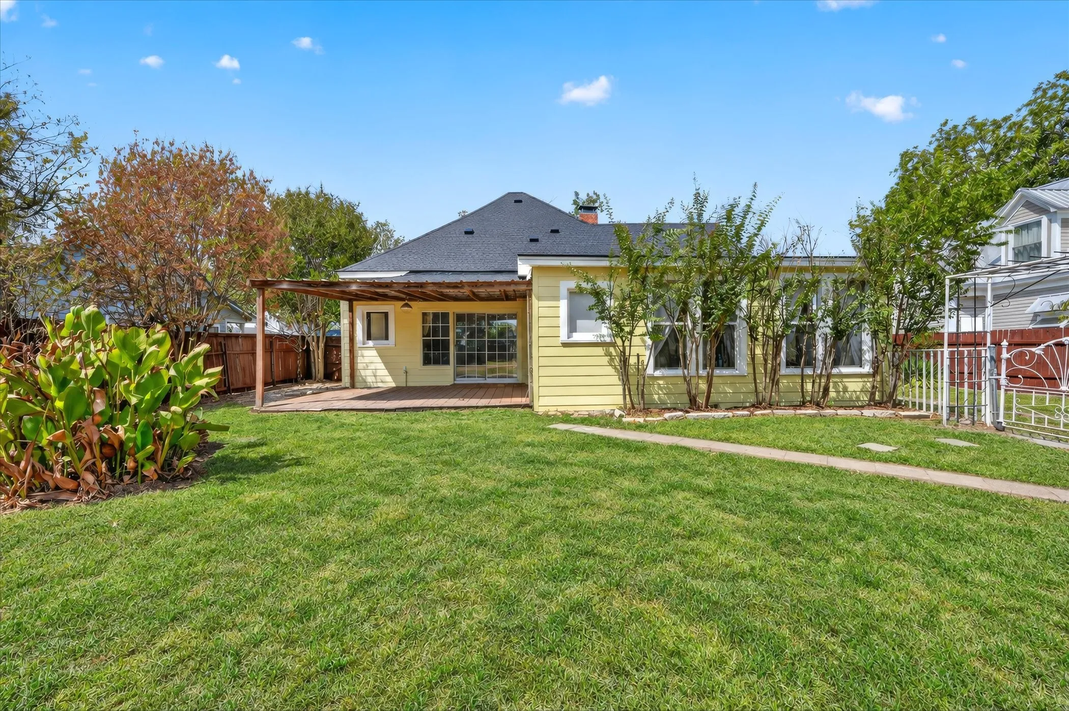 Expansive lawn with a paved pathway, leading to a brick patio with a wooden pergola
