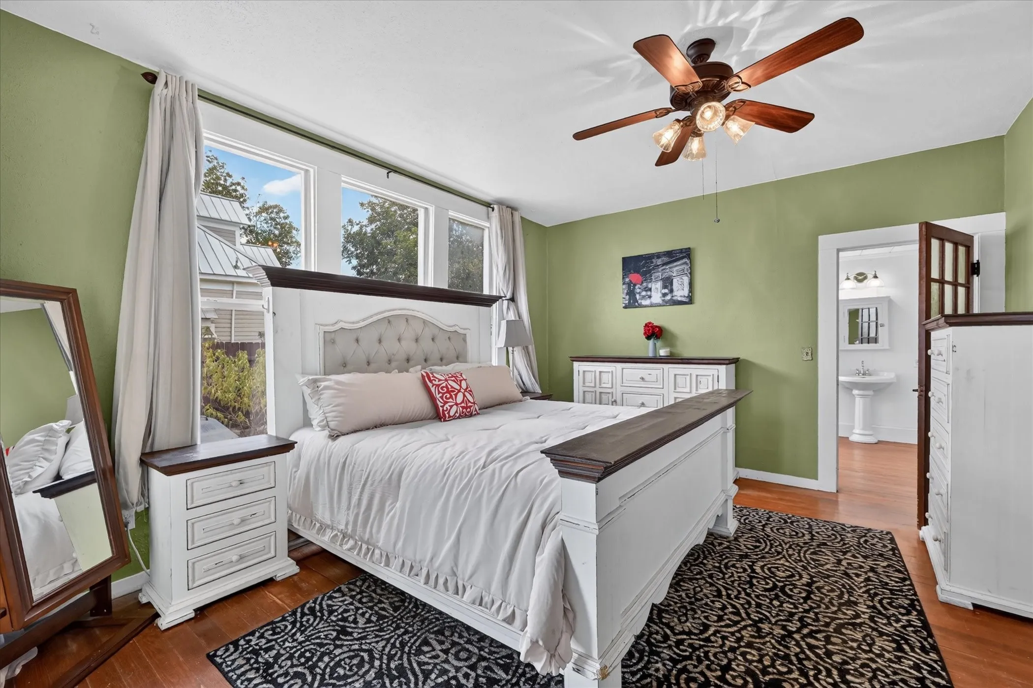 Wood-finish flooring with a multi-pane window array, a ceiling fan with integrated lighting, and a white pedestal sink with a framed mirror in the attached space