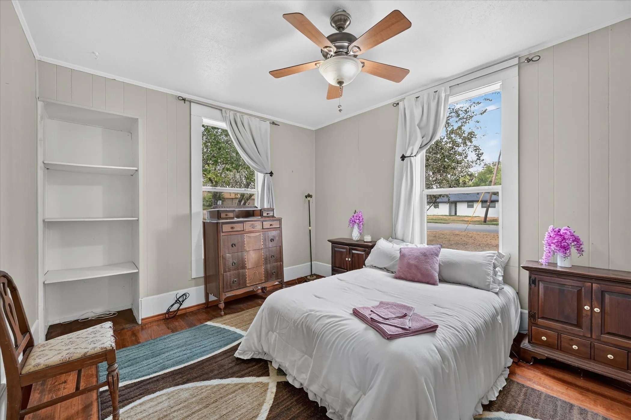 Hardwood flooring, painted paneling, built-in shelving, ceiling fan light fixture, and two windows with white trim