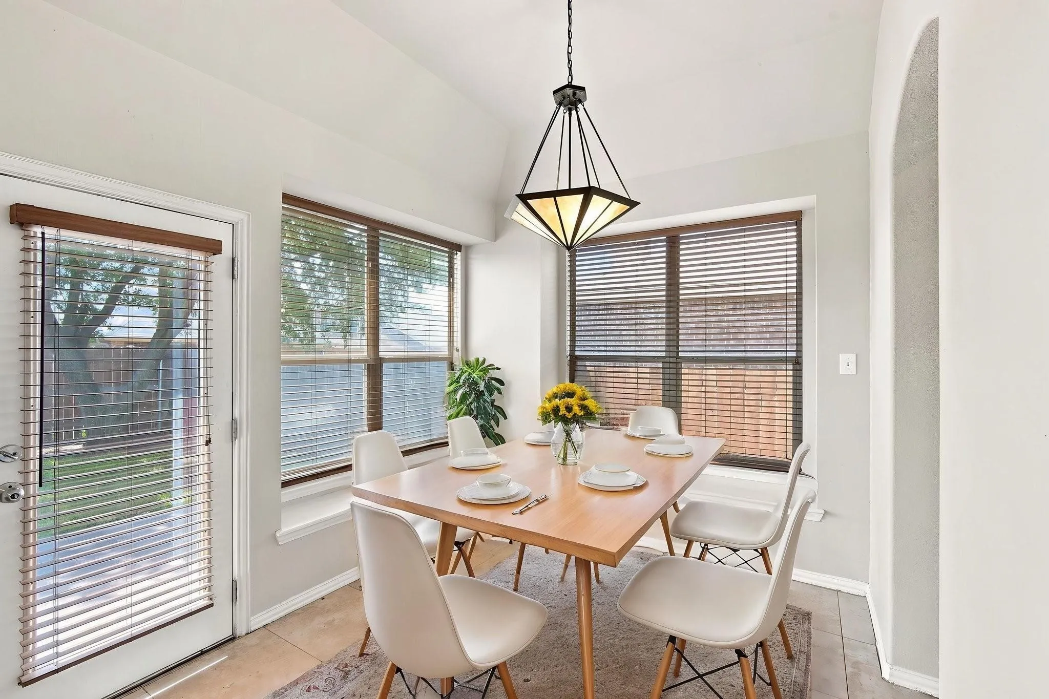 Vaulted ceiling with an architectural light fixture, bay window, tiled flooring, and an arched entryway