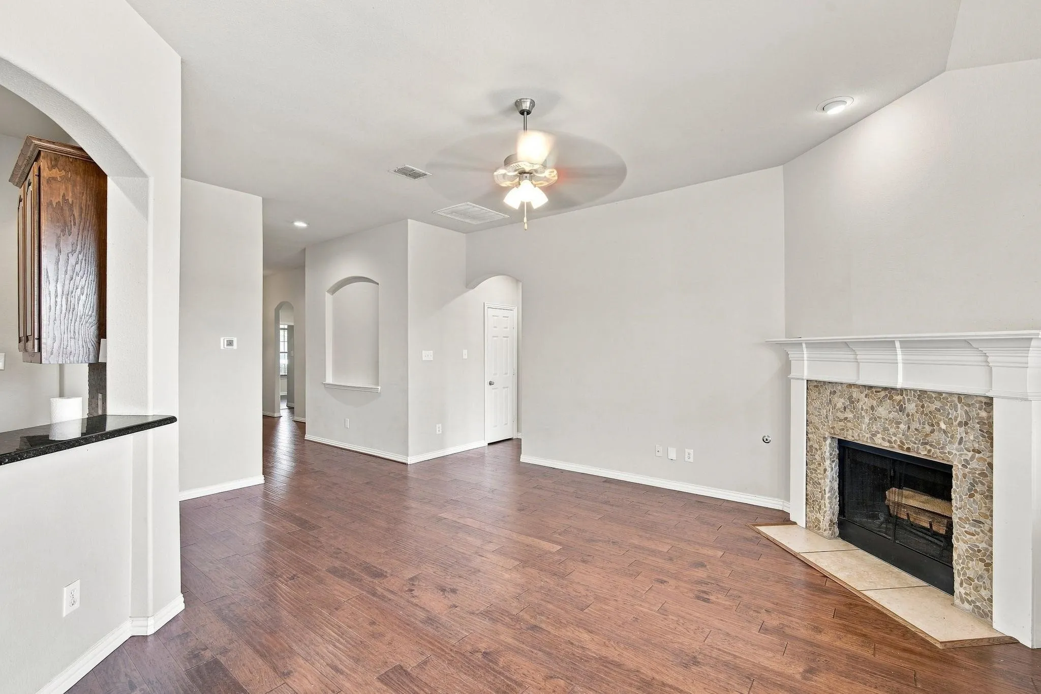 Spacious living area featuring wood-finish flooring, a fireplace with a stone surround, and an arched entryway