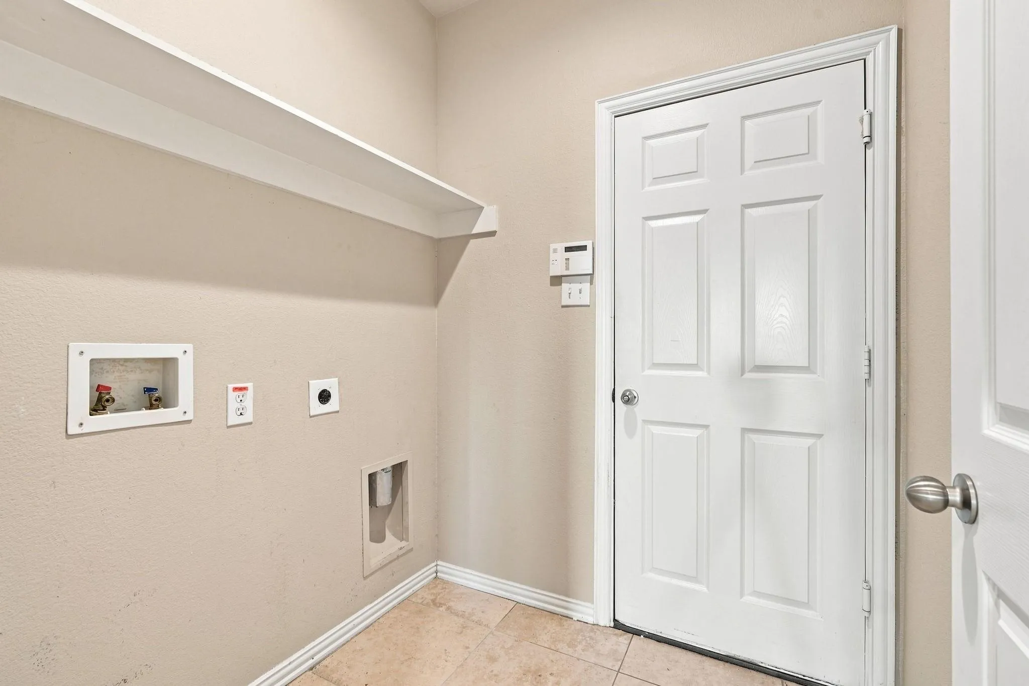 Built-in wall shelf, light-toned wall paint, tiled flooring, and a paneled door with round hardware