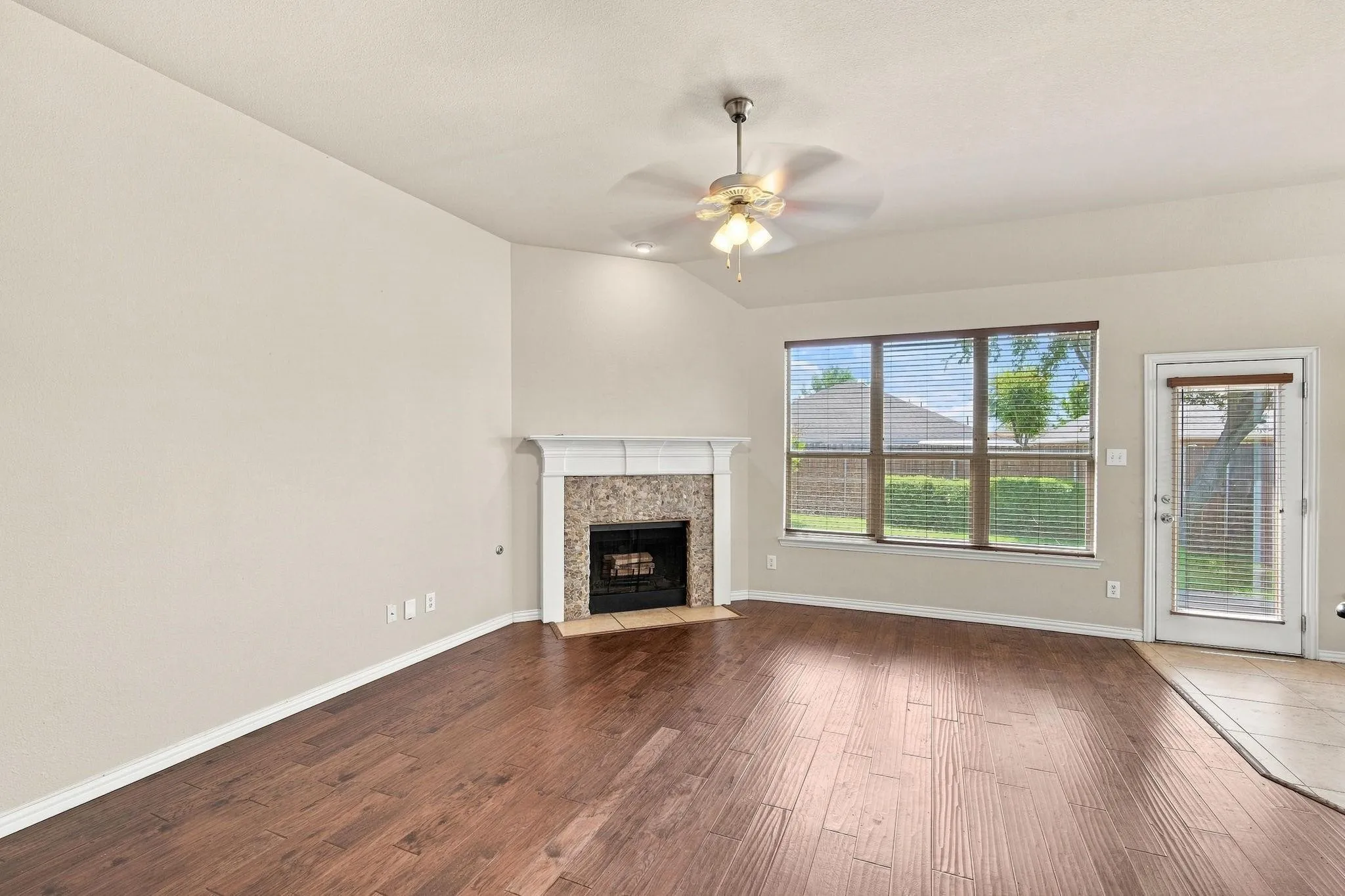 Wood-finish flooring throughout, vaulted ceiling, and a fireplace with stone surround