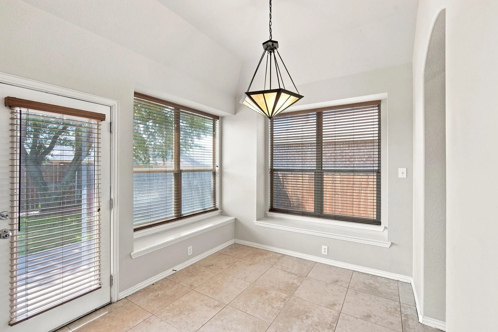 Vaulted ceiling, tiled flooring, geometric chandelier, two large windows with window sills, and an arched entryway