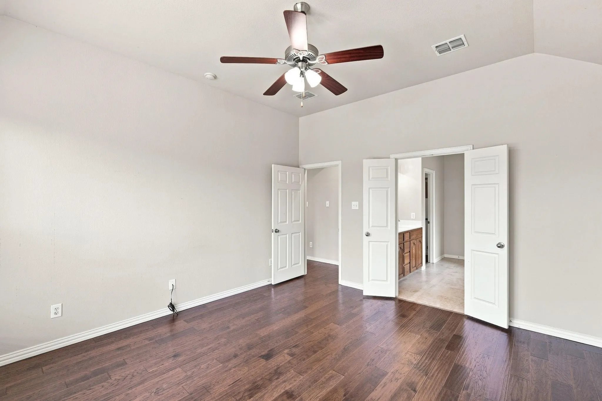 Wood-finish flooring, vaulted ceiling, ceiling fan with light fixture, and white interior doors