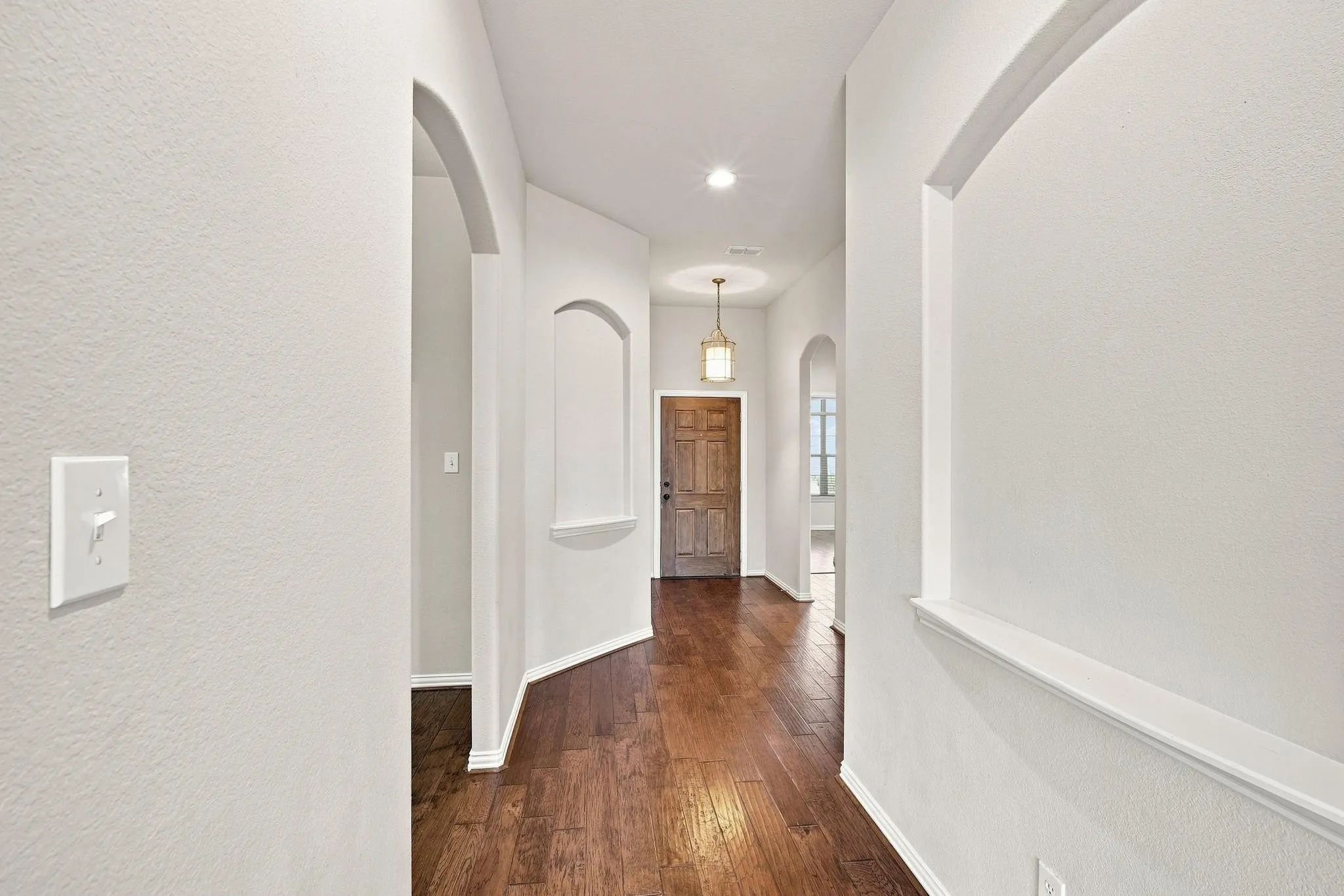 Arched doorways, wood-finish flooring, recessed lighting, and a decorative wall niche with a lower ledge