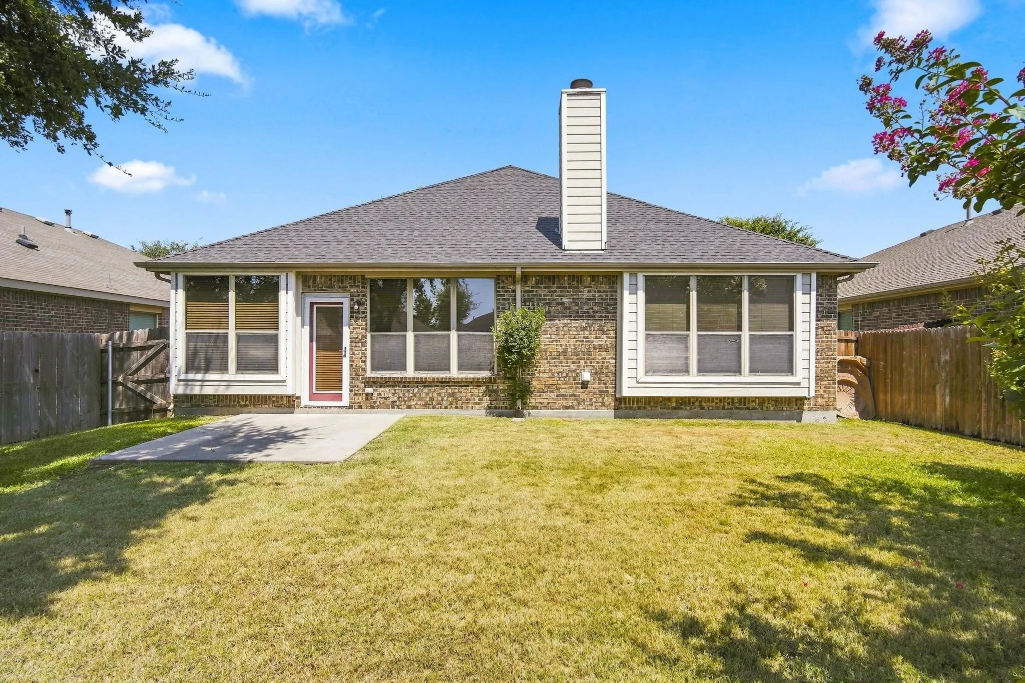 Expansive backyard featuring a patio, brick exterior, multiple windows, and a prominent chimney