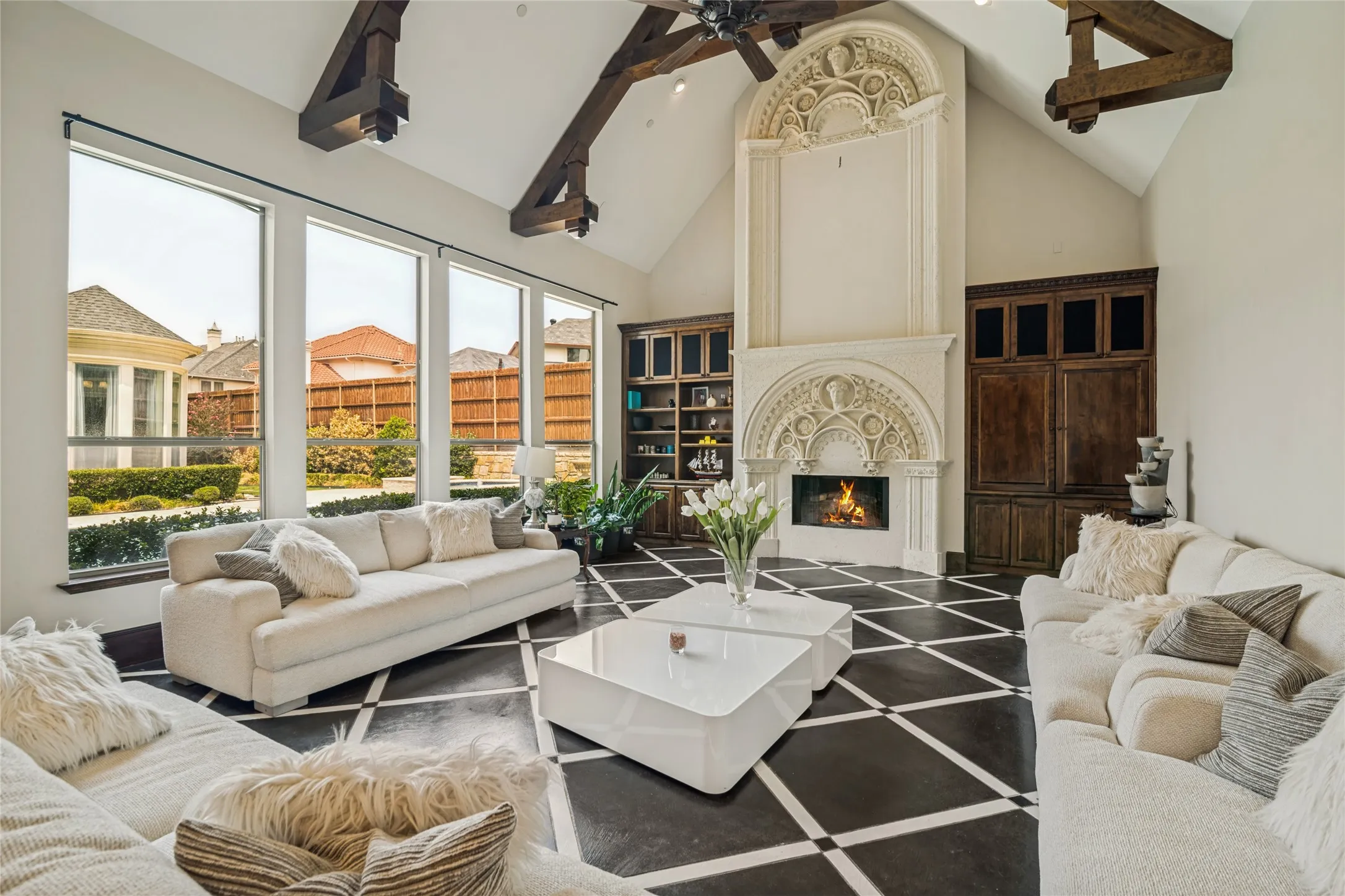 Vaulted ceiling with exposed wood beams, floor-to-ceiling fireplace with intricate carvings, built-in cabinetry, and large windows