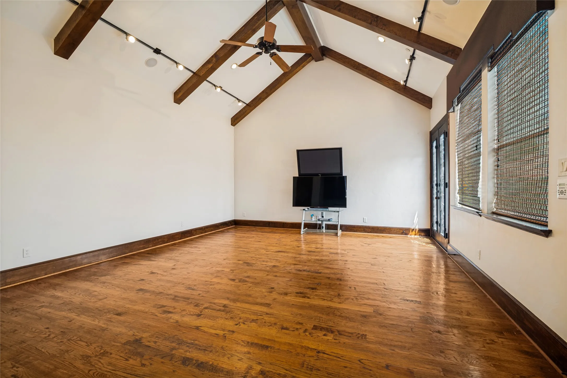 Vaulted ceiling with exposed wood beams, wood-finish flooring, ceiling fan, and track lighting