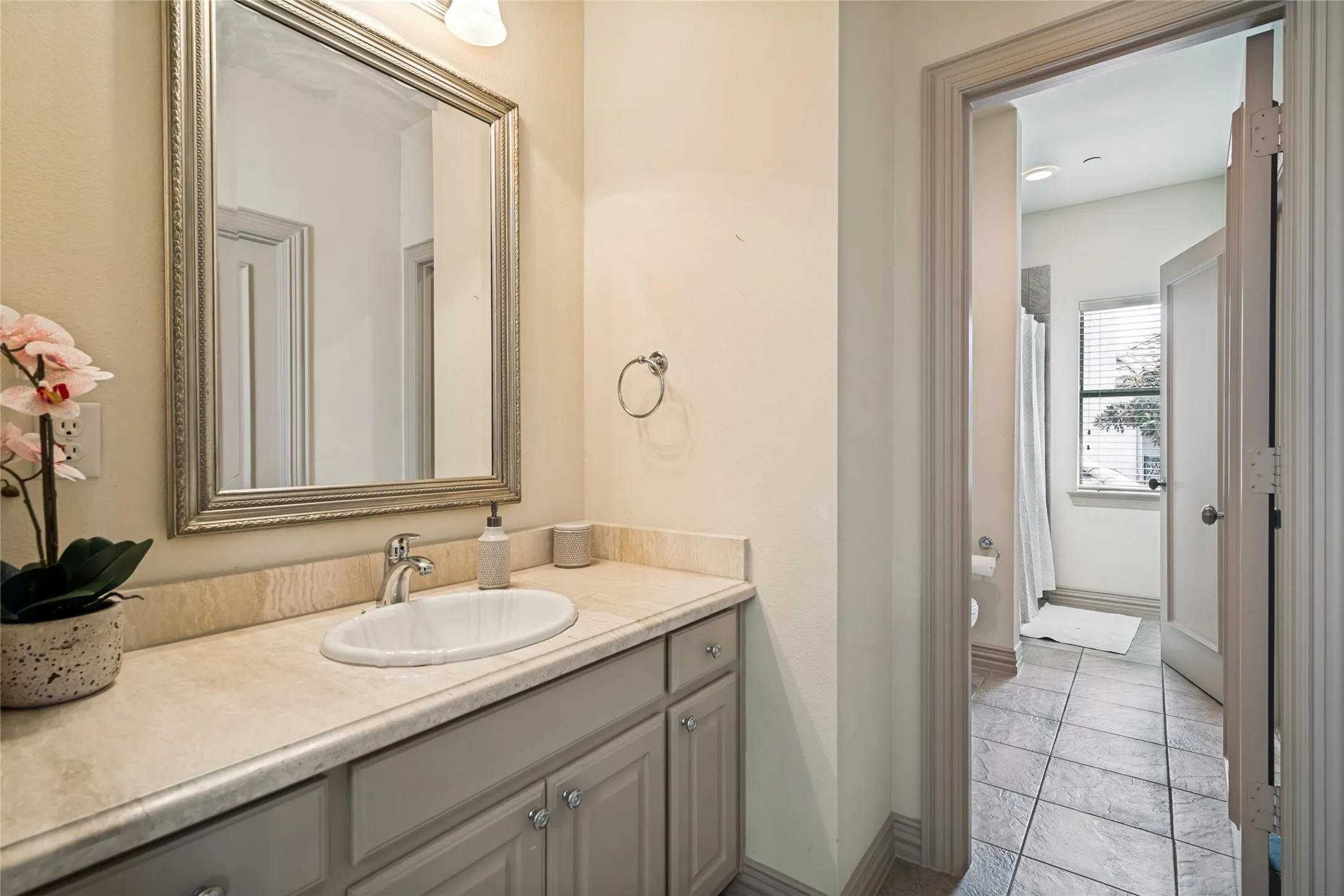 Elegant vanity featuring a round undermount sink, light-finish stone countertop, and polished chrome faucet accented by a framed mirror with brushed metal trim