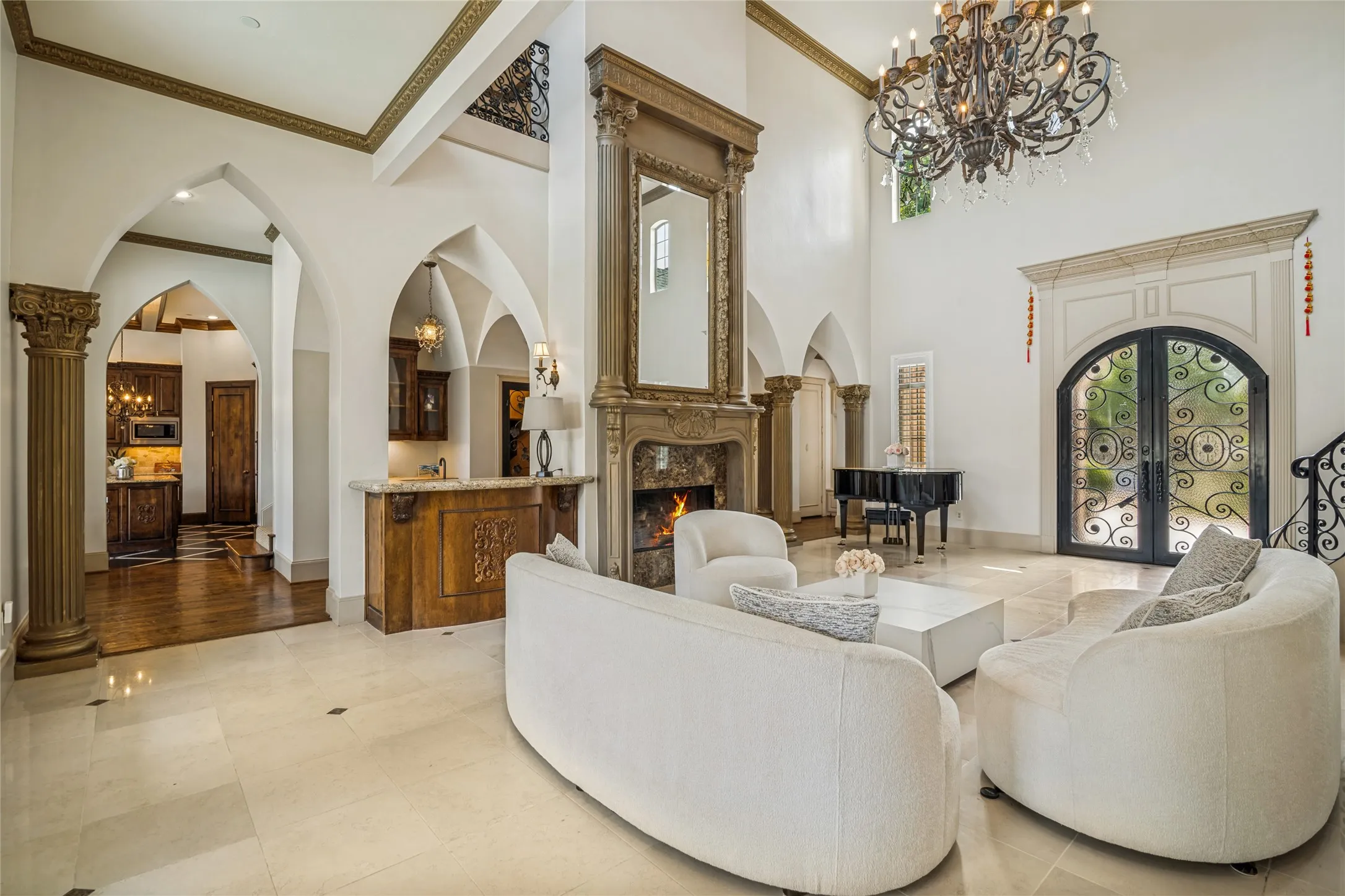 Grand living space featuring soaring ceilings, a substantial fireplace with an ornate mantel and mirror, stone flooring, and arched doorways with decorative columns