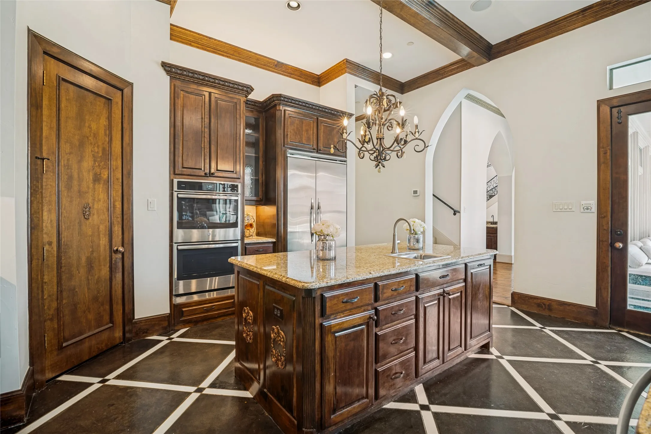 Gourmet kitchen featuring a central island with granite countertops, stainless steel appliances, dark wood cabinetry, and a decorative chandelier
