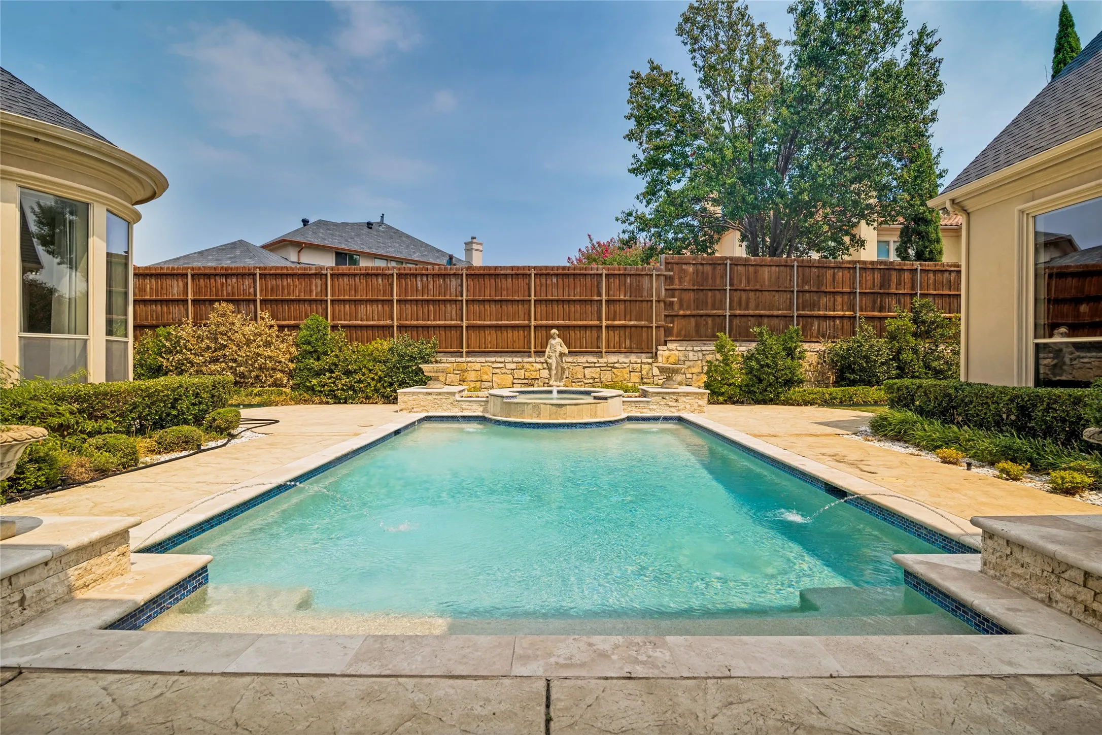 Expansive backyard featuring a rectangular swimming pool, stone patio surround, decorative fountain, and lush landscaping