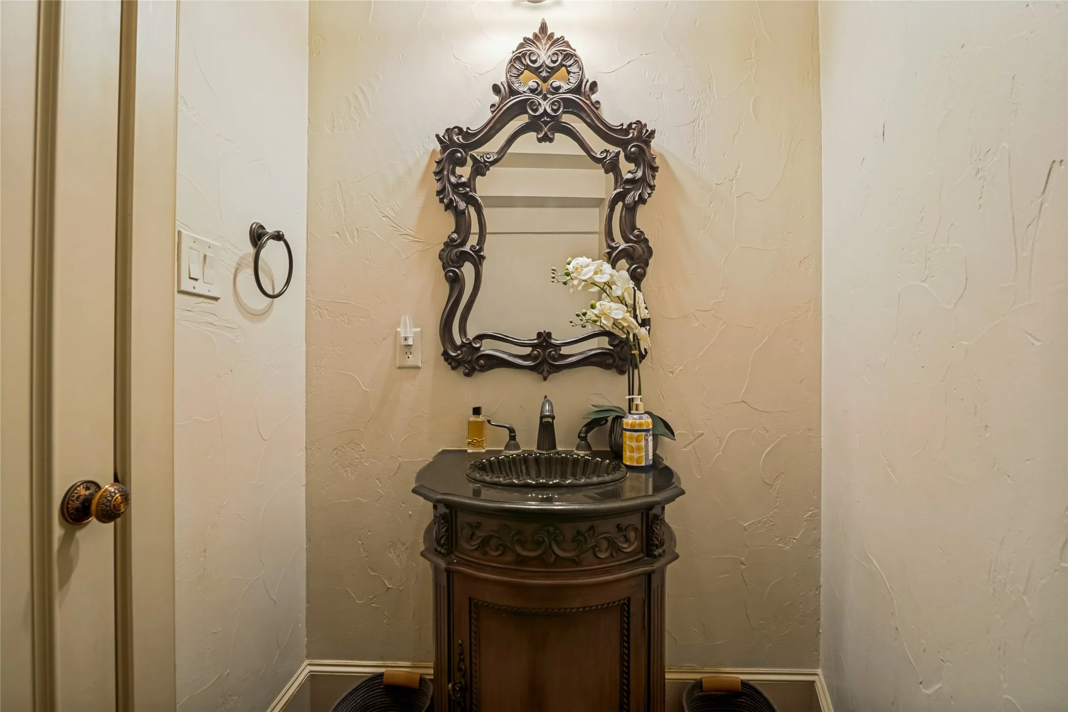 Ornate framed mirror and carved wood vanity with a dark countertop